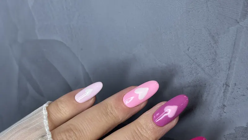 Pink almond nails with painted hearts on grey concrete